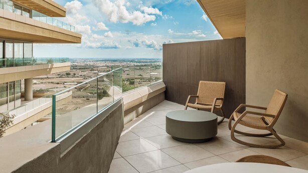 Un balcon moderne avec des garde-corps en verre, des fauteuils en osier et une table ronde.