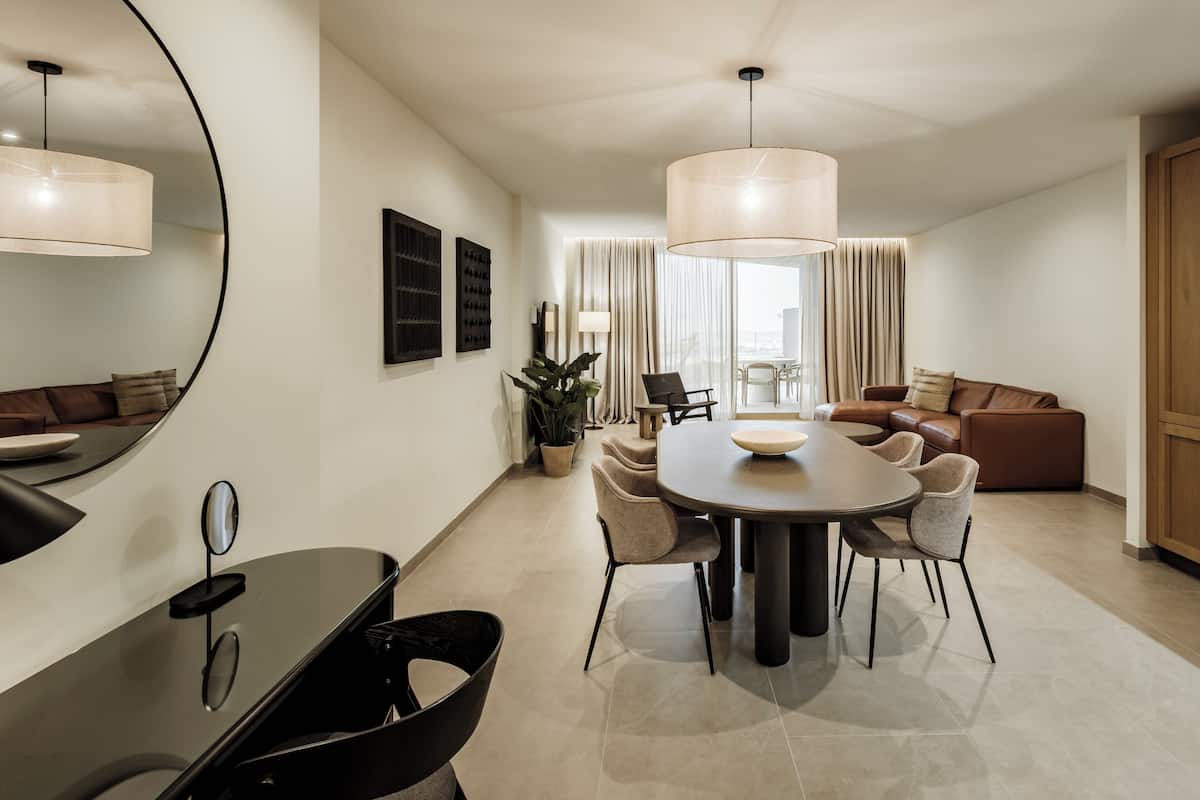A modern living room with a dining area, featuring a round table, chairs, a sofa, and a large mirror.