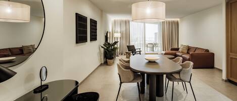 A modern living room with a dining area, featuring a round table, chairs, a sofa, and a large mirror.