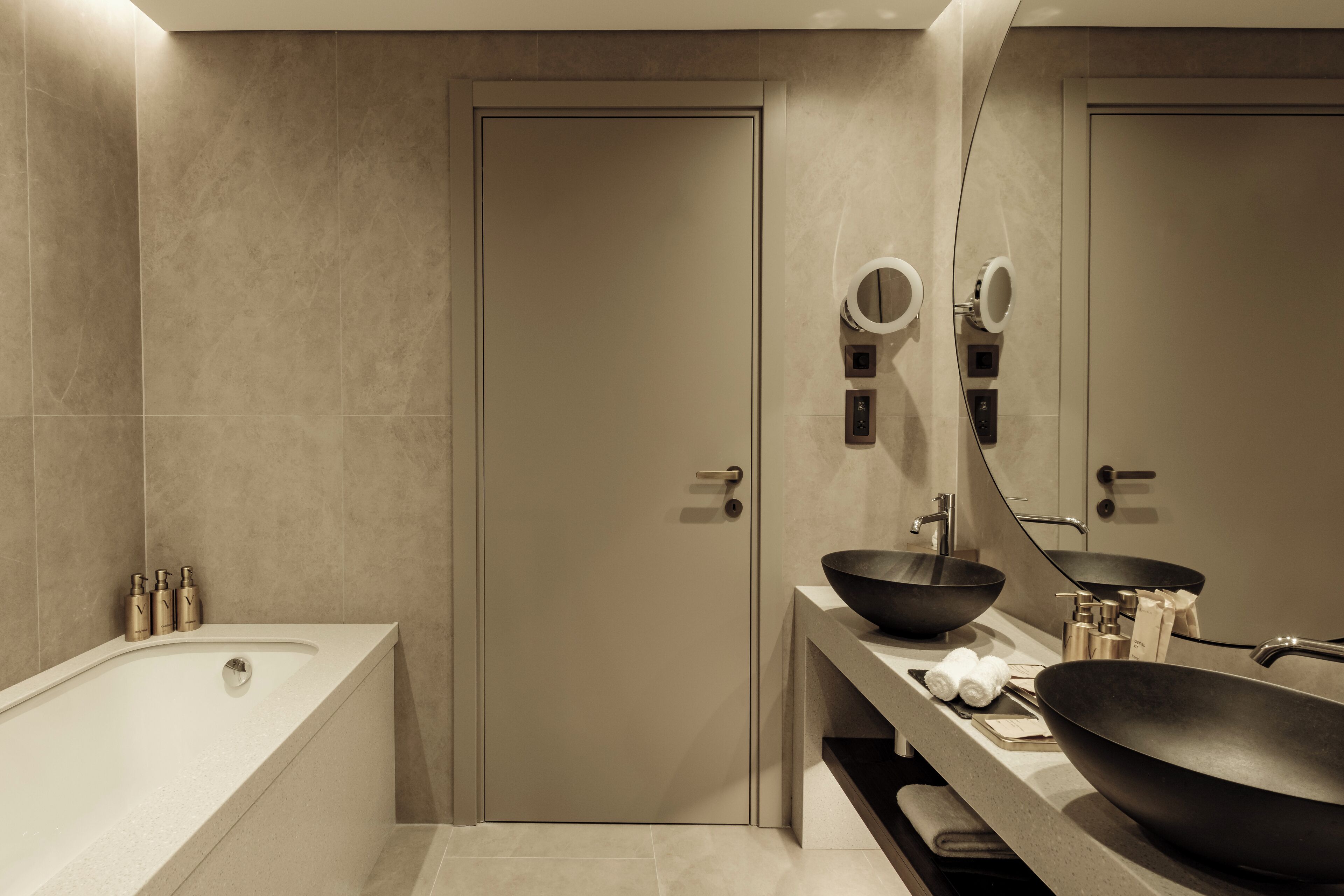 Een moderne badkamer met een badkuip, twee wastafels en een grote spiegel.