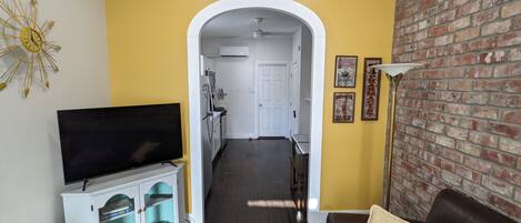 Una sala de estar con televisor, sofá, alfombra estampada y pared de ladrillo.
