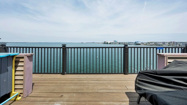 A wooden deck with a view of the water and distant cityscape. - New for 2025! Beached Themed Two Bedroom Direct Bayfront on 32nd Street (Ocean City)