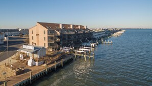 A waterfront hotel with a dock extending into the water, featuring multiple buildings with balconies and a small boat house. - New for 2025! Beached Themed Two Bedroom Direct Bayfront on 32nd Street (Ocean City)