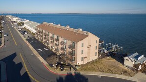 A beachfront hotel with a parking lot, a road with yellow lines, and a view of the ocean. - New for 2025! Beached Themed Two Bedroom Direct Bayfront on 32nd Street (Ocean City)