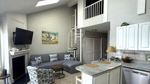 A modern kitchen with a central island, a dining area with a white table, and a living room with a sofa and a fireplace. - New for 2025! Beached Themed Two Bedroom Direct Bayfront on 32nd Street (Ocean City)