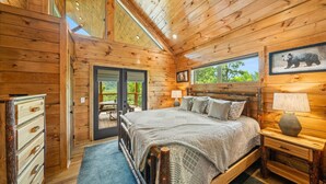 A wooden cabin bedroom with a bed, bedside table, and a view of the outdoors.