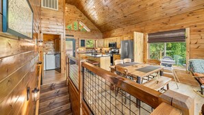A wooden cabin interior with a kitchen, dining area, and a staircase leading to a loft.