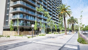 Un immeuble moderne de grande hauteur, doté de nombreux balcons, d’un espace extérieur couvert et de palmiers.