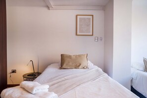 A hotel room with a bed, a bedside table with a lamp, a framed picture on the wall, and a power outlet.