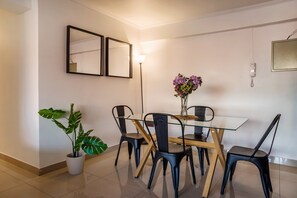 Un comedor con una mesa de vidrio, sillas negras, una planta en maceta y un jarrón de flores.