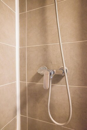 Ducha con manguera flexible y grifo cromado sobre paredes de azulejos color crema.