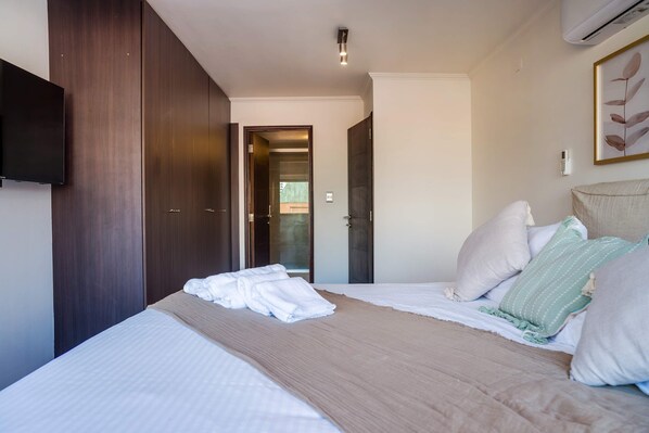 Habitación de hotel con cama, televisión de pantalla plana, puerta que da a un balcón y aire acondicionado de pared.