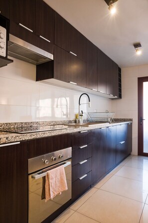 Una cocina moderna con gabinetes oscuros, una campana extractora de acero inoxidable, un horno empotrado y un salpicadero de azulejos.