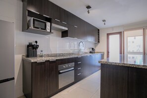 A modern kitchen with dark cabinetry, a stainless steel oven, a microwave, and a coffee maker. - Spacious 2BR/2BA Apt. in the Heart of Las Condes (Las Condes)