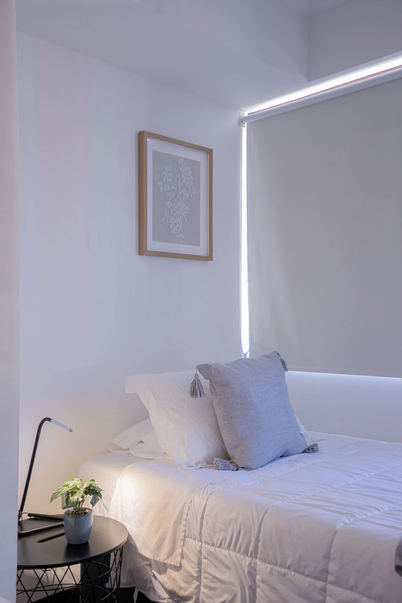 Een minimalistische slaapkamer met een bed, nachtkastje, lamp en een lijst met een foto aan de muur.