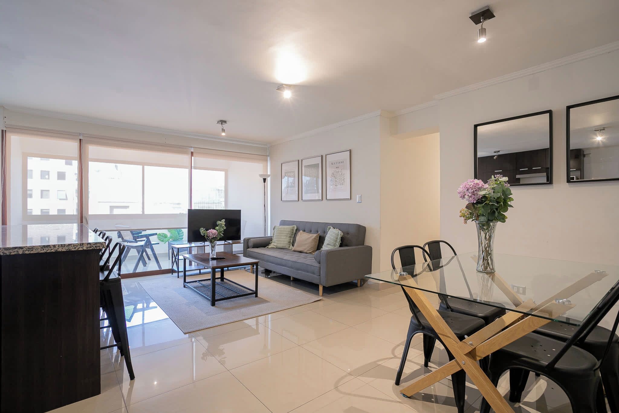 A modern living room with a sofa, a glass dining table, and a TV.