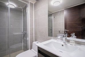 A modern bathroom with a glass shower enclosure, a white sink with a mirror, and a dark wooden vanity. - Spacious 2BR/2BA Apt. in the Heart of Las Condes (Las Condes)