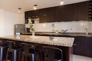Una cocina moderna con armarios de madera oscura, encimera de granito, refrigerador de acero inoxidable y una zona de bar con taburetes.