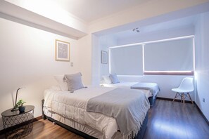A modern bedroom with a bed, bedside tables, a chair, and a window with blinds. - Spacious 2BR/2BA Apt. in the Heart of Las Condes (Las Condes)