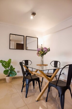 A modern dining area with a glass table, black chairs, and a potted plant.