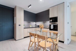 Eine moderne Küche mit einem Glastisch und Holzstühlen, einem Einbauofen und einem dunkel gefärbten Schrank.
