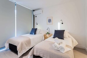 Ein Hotelzimmer mit zwei Betten, einem Nachttisch, einer kleinen Pflanze und einem gerahmten Bild an der Wand.