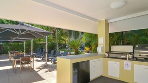 An outdoor kitchen area with a grill, a refrigerator, and a dining setup with chairs and umbrellas.
