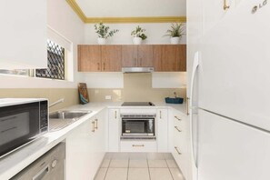 A compact kitchen with white cabinetry, a built-in oven, a microwave, and a refrigerator.