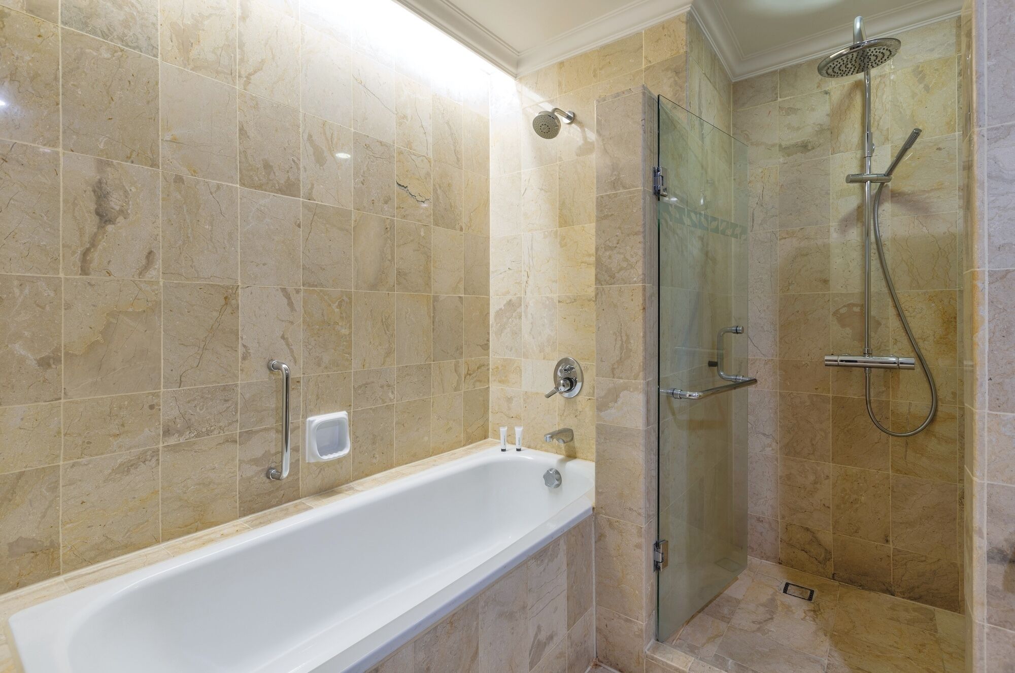 Une salle de bain avec une baignoire, une douche à parois de verre et un mur recouvert de carreaux de marbre.