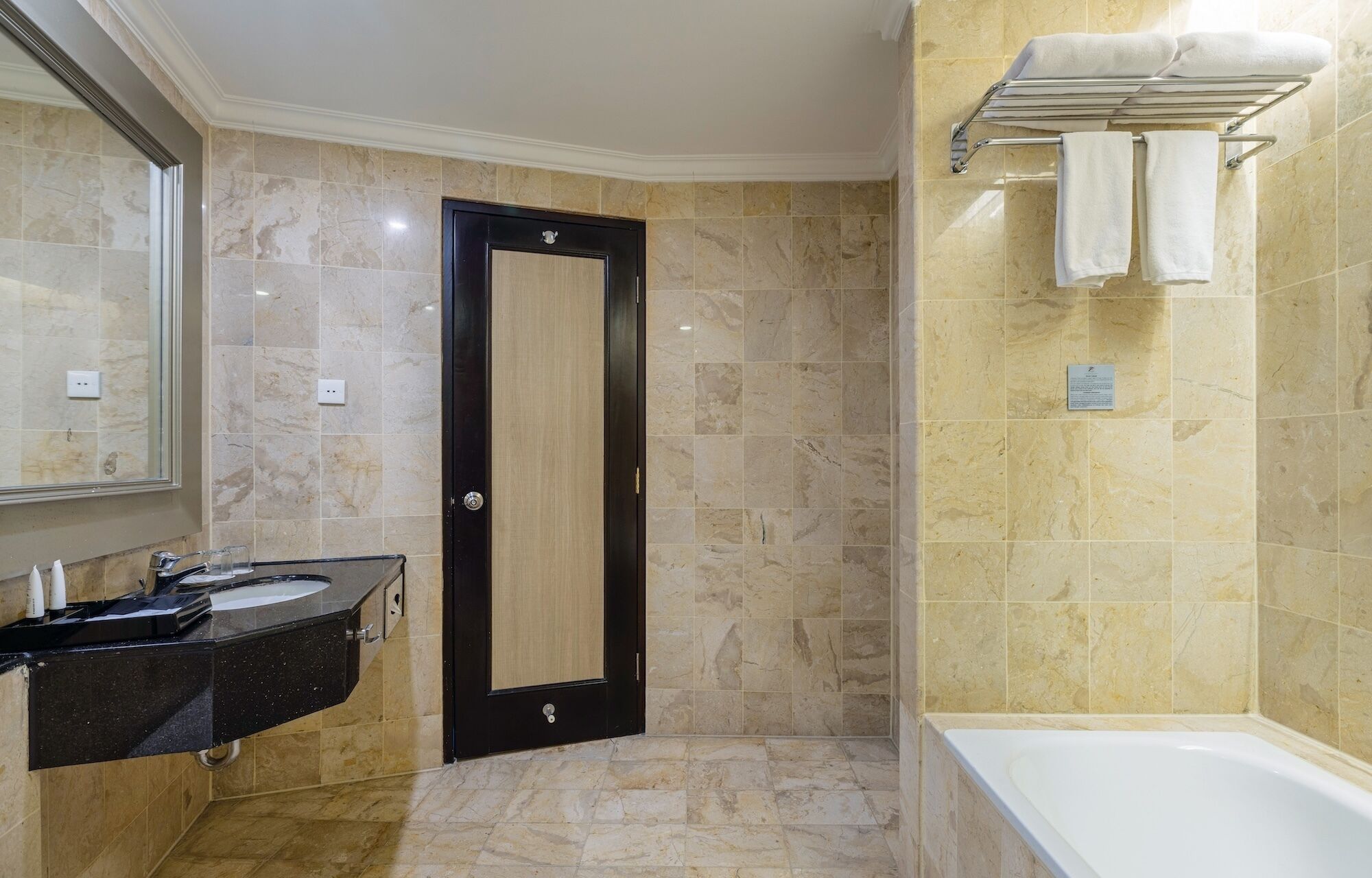 A bathroom with a black door, a sink with a mirror, and a bathtub.