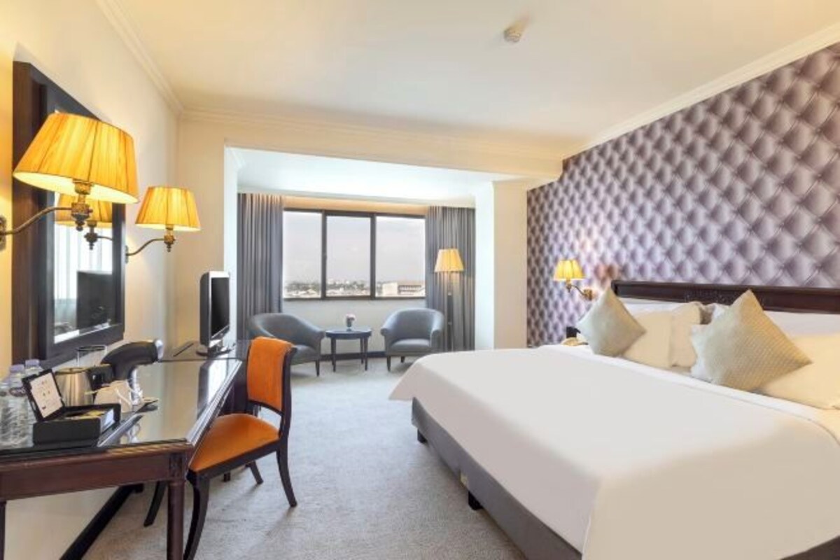 Een hotelkamer met een groot bed, een bureau met een computer, twee stoelen, een televisie en uitzicht op de stad.