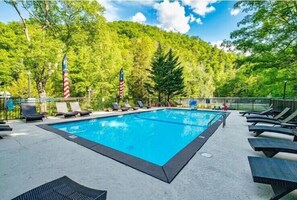 Una piscina rettangolare con lettini e bandiere americane, circondata da alberi.