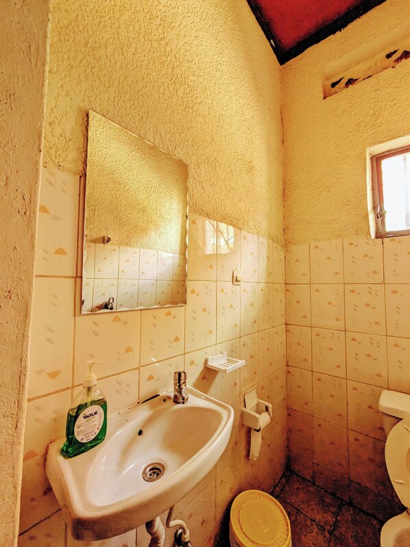 A small bathroom with a sink, mirror, toilet, and a window. - Rand's House I Homestay (Ruhengeri)