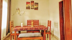 A dining area with a wooden table and chairs, a chandelier, and wall-mounted electrical outlets. - Rand's House I Homestay (Ruhengeri)