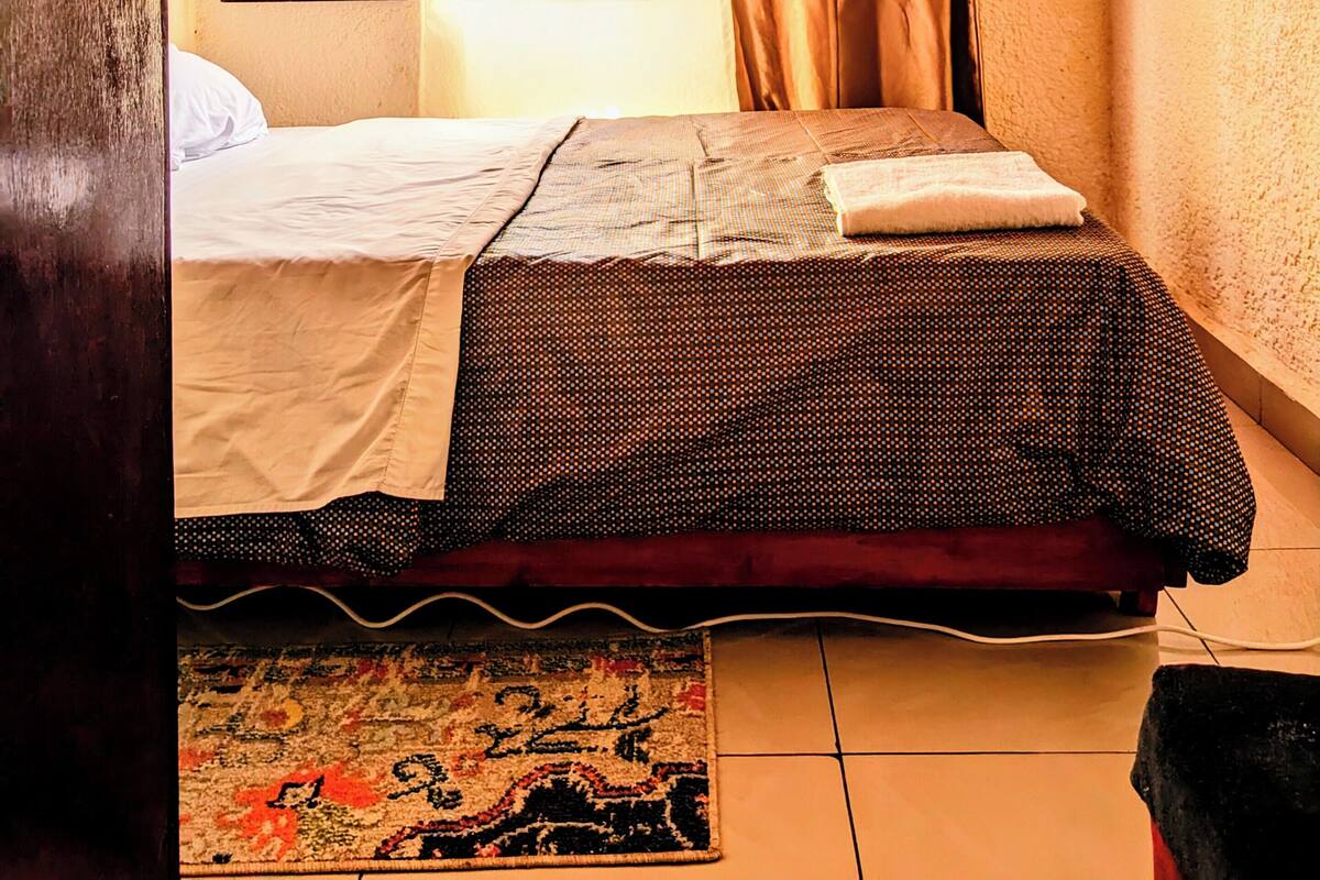 A bedroom with a bed, a window with curtains, a bedside table, and a rug.