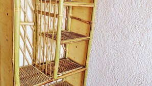 A bamboo shelf unit with multiple shelves and a small white object on the top shelf. - Rand's House I Homestay (Ruhengeri)