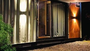 Una casa moderna con un amplio ventanal corredero, una puerta de madera y un toldo rojo.