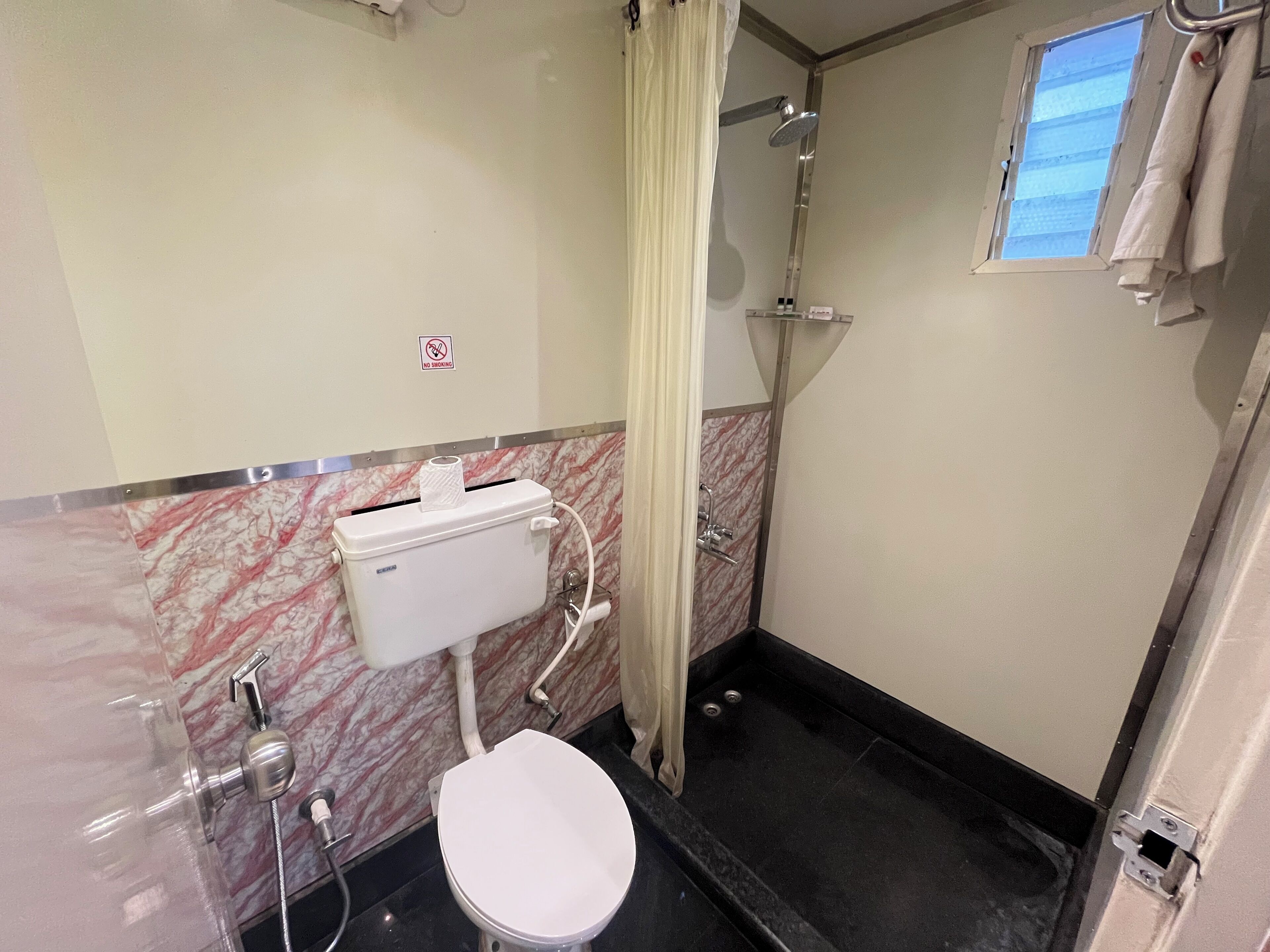 A compact bathroom with a toilet, shower, and a no-smoking sign on the wall.