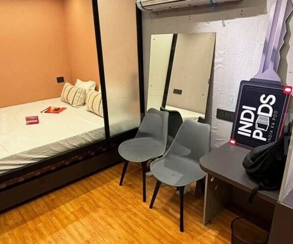 Une petite pièce comprenant un lit, deux chaises, un petit bureau et un miroir.