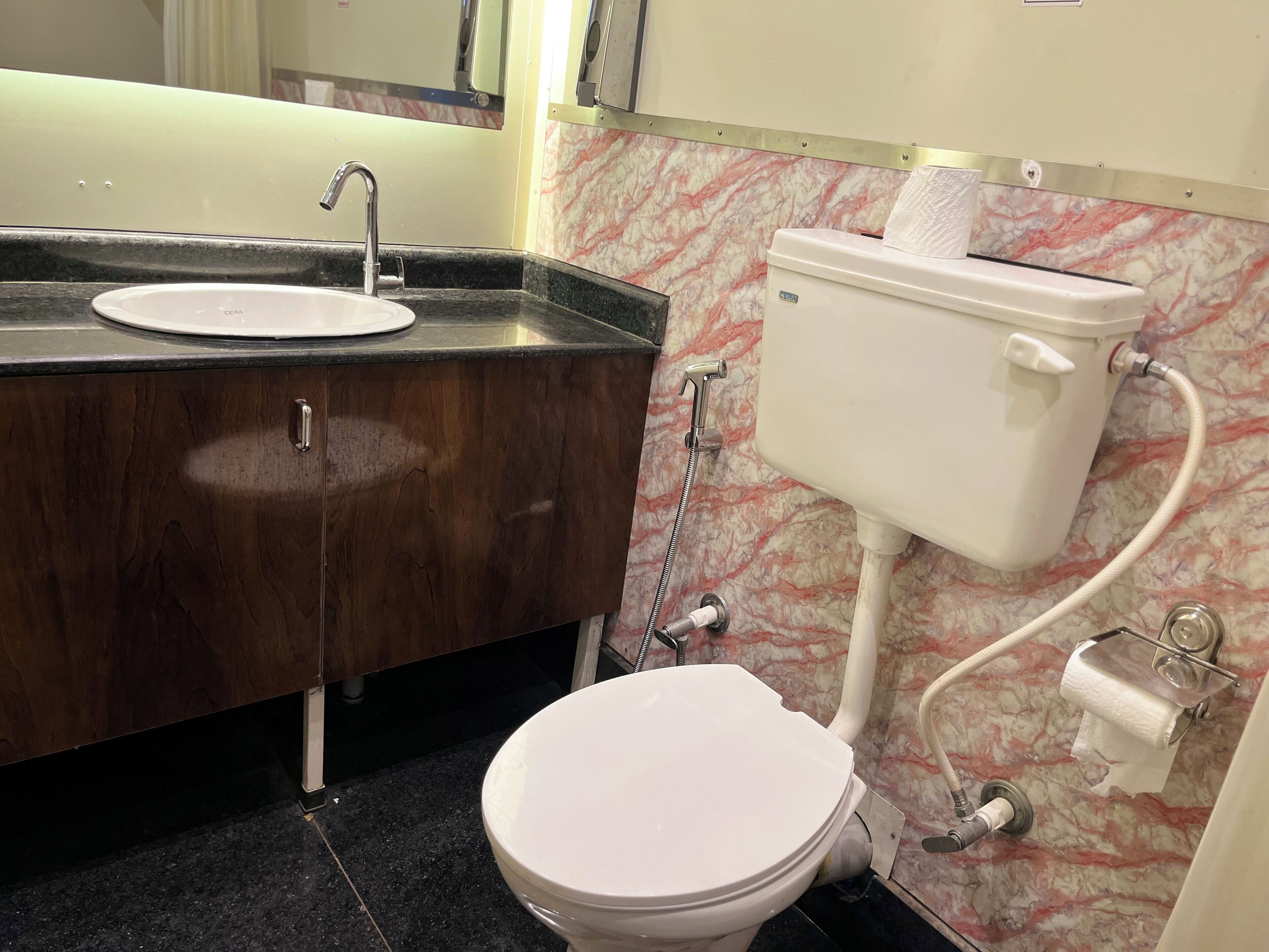 A bathroom with a marble wall, a sink with a CERA brand faucet, a toilet, and a paper towel dispenser.