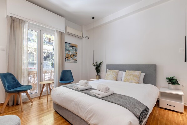 Una habitación de hotel moderna con una cama grande, dos sillas, una mesita y un balcón con cortinas.