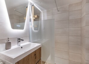 Un baño moderno con un espejo grande, un lavabo blanco y una cabina de ducha.