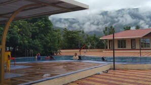 Une piscine dotée d’une zone couverte, un bâtiment avec un toit rouge et un paysage montagneux en arrière-plan.