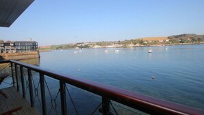 A waterfront view with a wooden deck and a glass railing overlooking calm water with boats. - Tobys Quay (Falmouth)