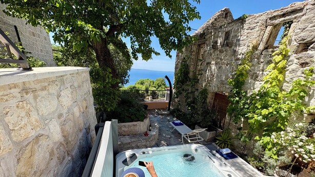 A swimming pool with a view of the sea, surrounded by stone walls and greenery.