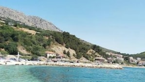 A coastal scene with clear blue water, rocky hills, and a few buildings in the background.