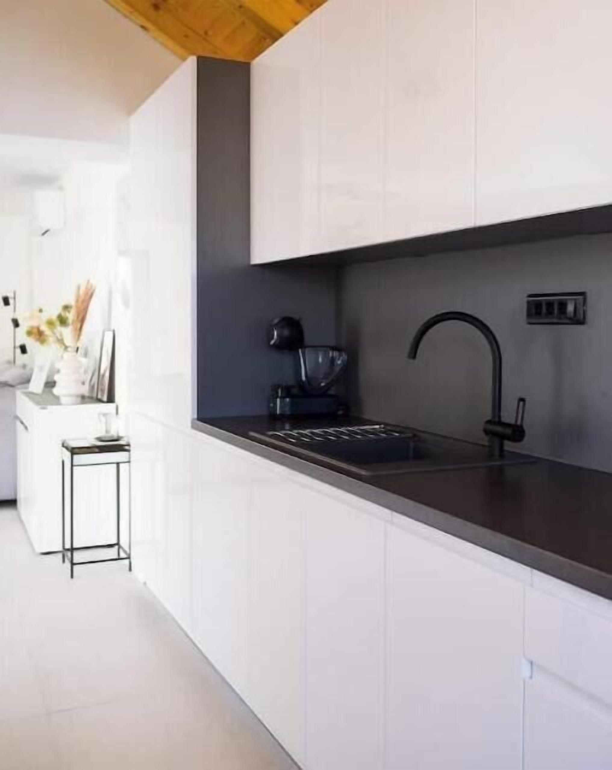 A modern kitchen with white cabinets, a black countertop, and a black faucet.