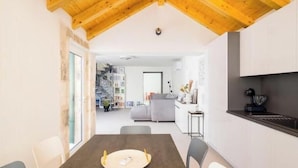 A modern kitchen with wooden beams, a dining table with chairs, and a view into a living area with a staircase.