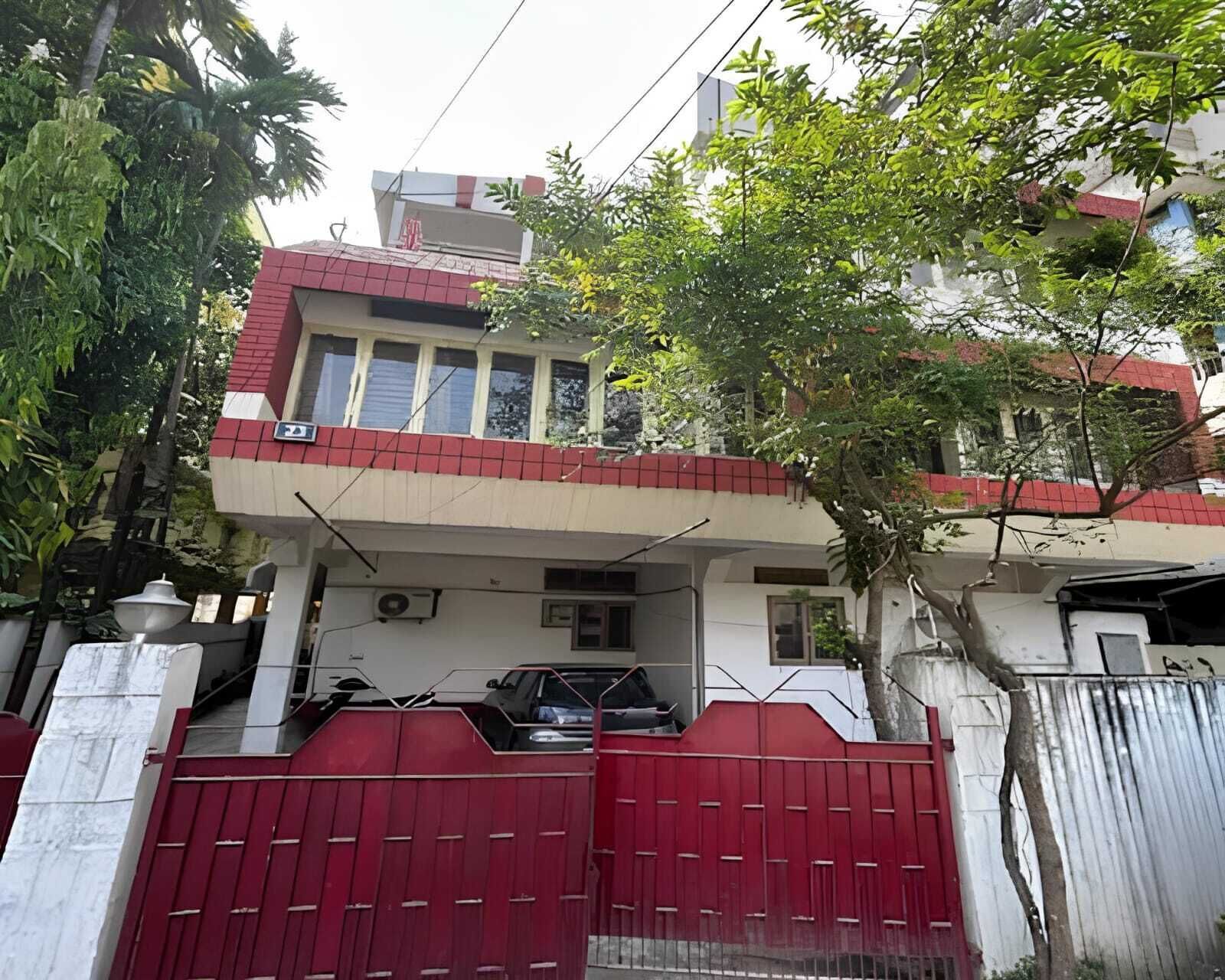 A two-story house with a red and white facade, a gated entrance, and a tree in the foreground.