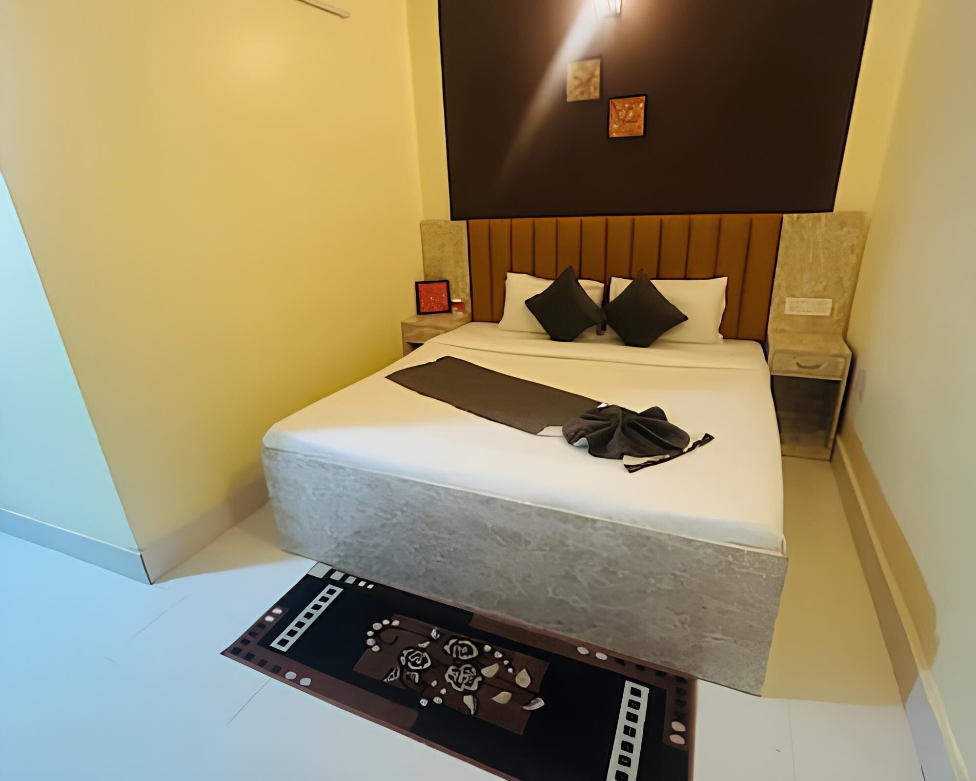 A neatly made bed with a white comforter, two black pillows, and a brown blanket. There is a small bedside table with a red object on it.